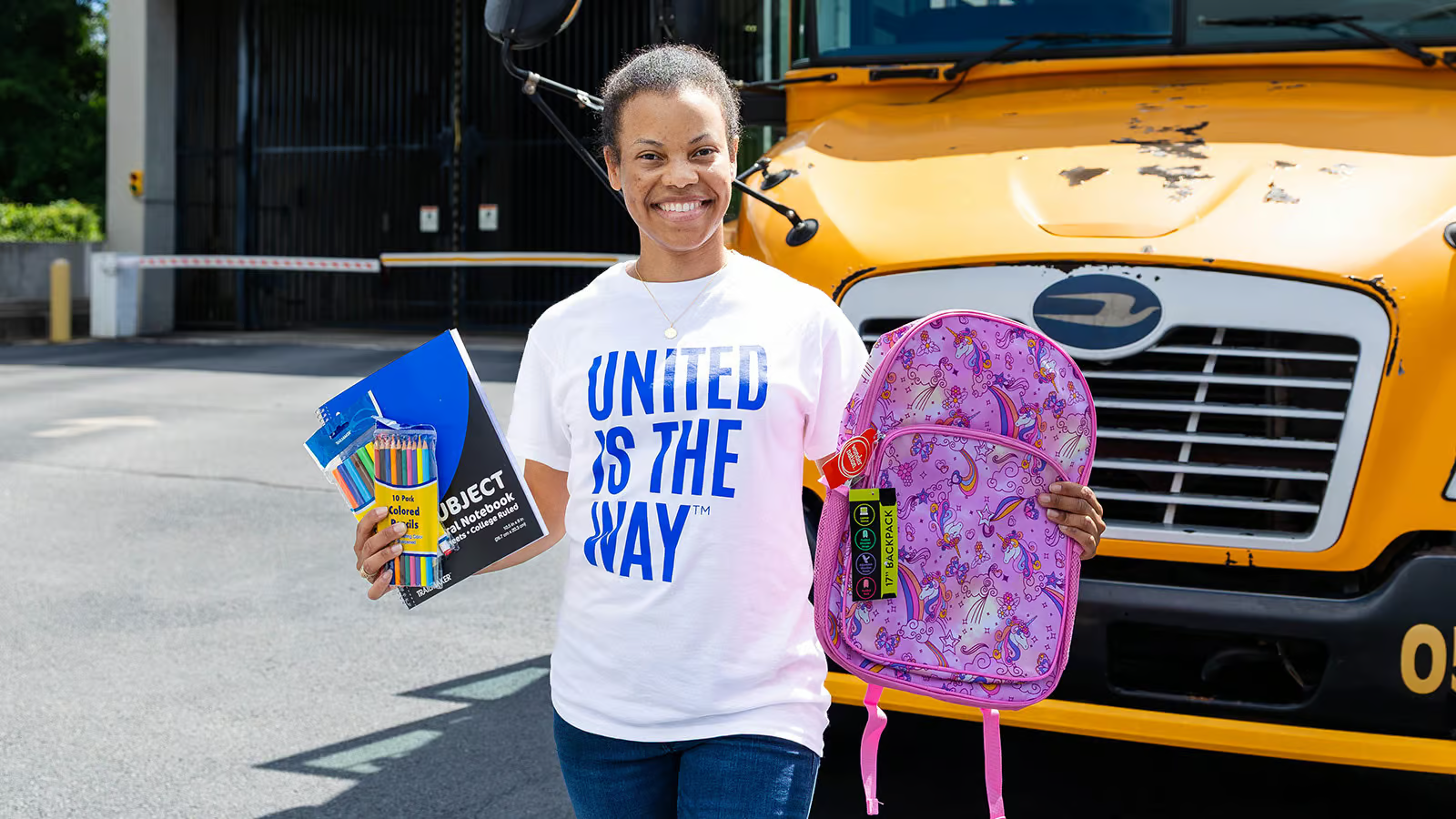 A volunteer holding school supplies beside a school bus
